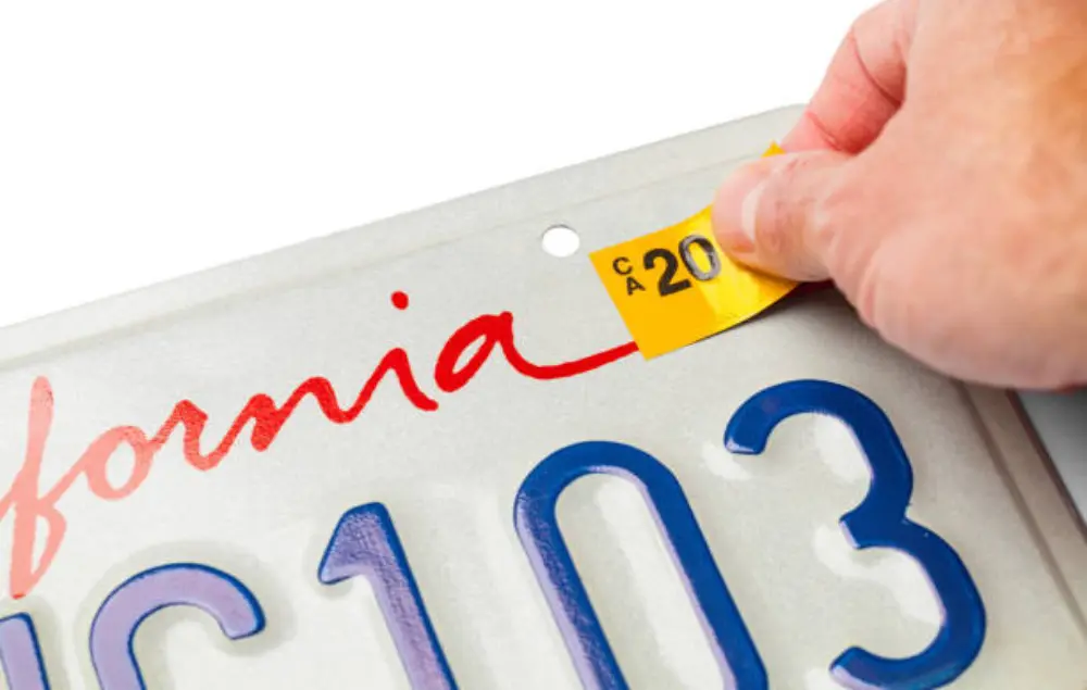A person holding up a yellow sticker on the back of a license plate.