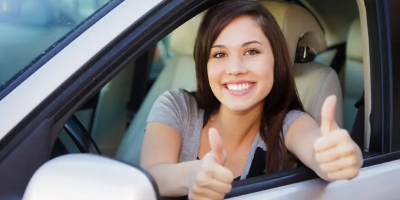 A woman sitting in her car giving the thumbs up.